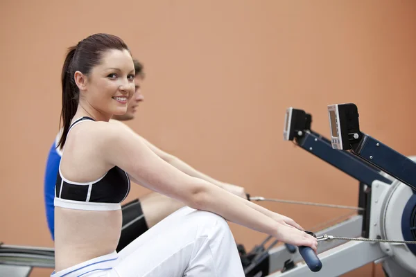 Mujer feliz con su novio usando un remador en un gimnasio —  Fotos de Stock