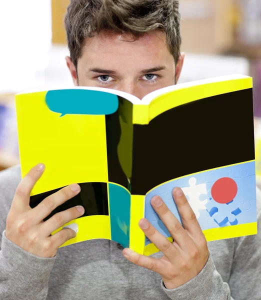 Männlicher Student, der in einer Buchhandlung steht und sein Gesicht hinter einem Bo versteckt — Stockfoto