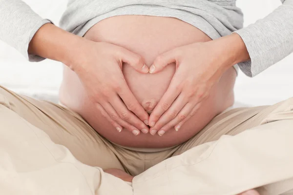 关闭一个怀孕的女人在做心脏标志在她的肚子上的 — 图库照片