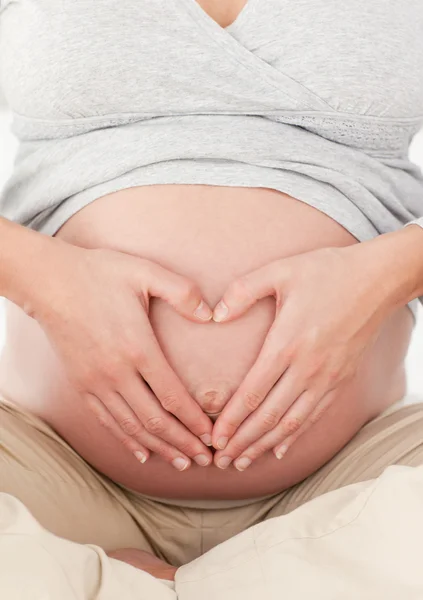 Primer plano de una futura mamá haciendo un signo de corazón en su vientre —  Fotos de Stock