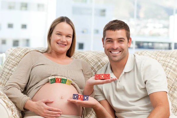 Happy future parents holding cubes sitting in the sofa — Stock Photo, Image