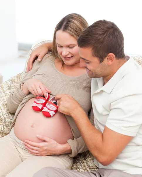 Handsome future dad putting baby shoes his wife's belly — Stock Photo, Image