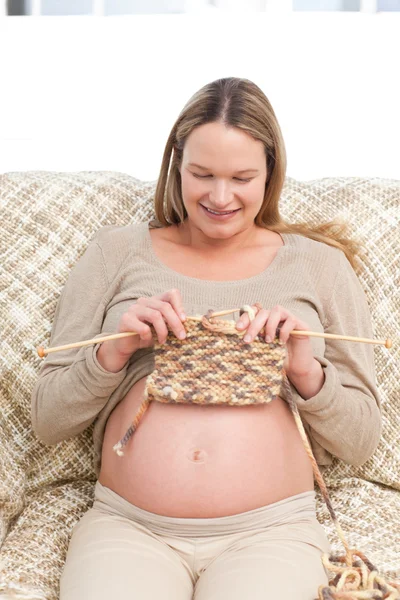 Niedliche zukünftige Mutter strickt sitzend auf dem Sofa — Stockfoto