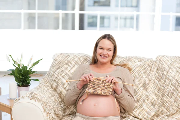 Ładna kobieta knitting dla jej przyszłości dziecko siedzi na kanapie — Zdjęcie stockowe