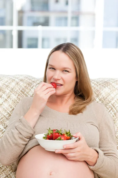 Vážné budoucí maminka jíst jahody sedí na pohovce — Stock fotografie