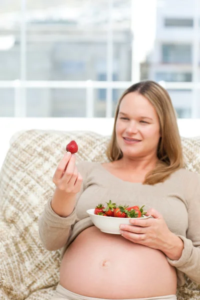 Urocza kobieta w ciąży patrząc na truskawki podczas relaksu — Zdjęcie stockowe