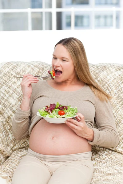 Mulher grávida devorando uma salada no sofá — Fotografia de Stock