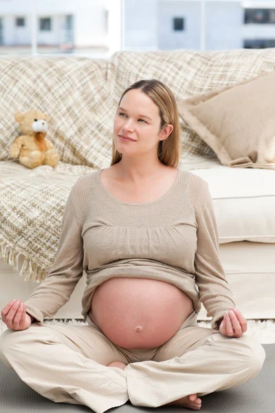 Беременная женщина, занимающаяся йогой, сидит на полу — стоковое фото