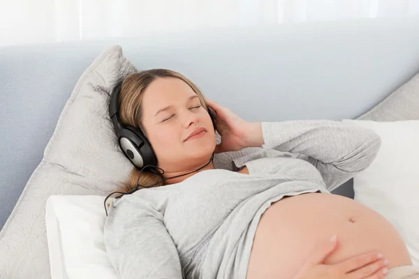 Bela futura mãe ouvindo a música deitada em uma cama — Fotografia de Stock