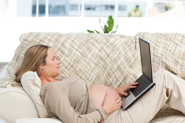 Mulher grávida caucasiana trabalhando em um laptop enquanto relaxa — Fotografia de Stock