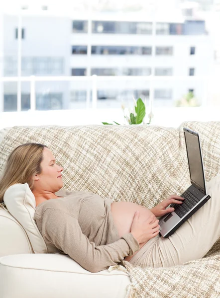 Mujer embarazada relajada usando su portátil en el sofá —  Fotos de Stock