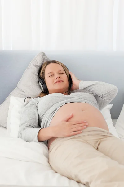 Futura mãe pacífica com fones de ouvido em mentir em uma cama — Fotografia de Stock
