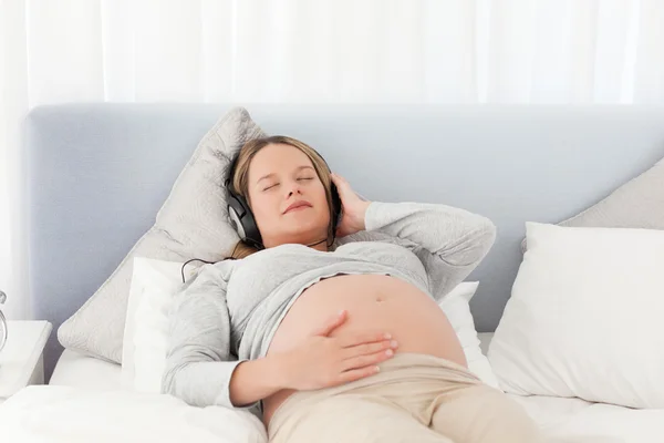 Relaxed future mom listening to the music on a bed — Stock Photo, Image