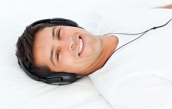 Hombre guapo escuchando la música tumbado en su cama —  Fotos de Stock