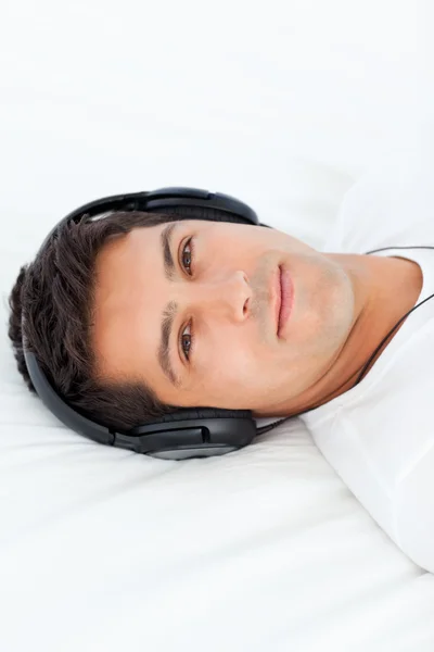Poważny człowiek z słuchawkami na leżąc na łóżku — Zdjęcie stockowe