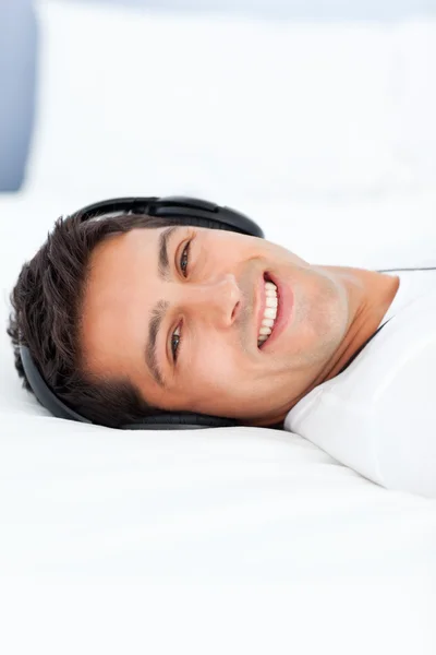 Hombre alegre escuchando música con auriculares acostados en su cama — Foto de Stock
