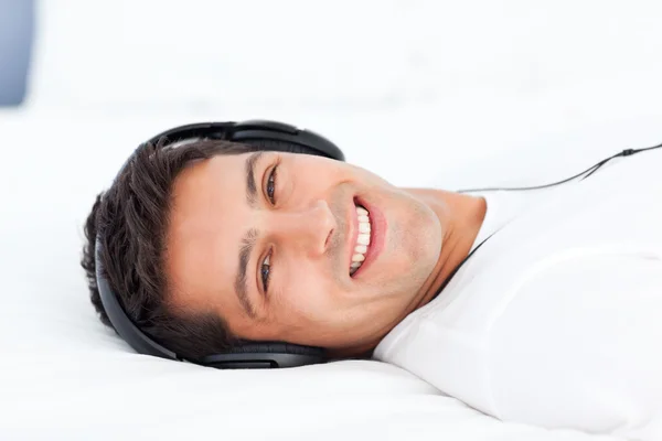 Portrait of a happy man listening music lying on his bed — Stock Photo, Image