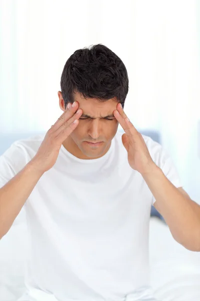 Handsome man having a headache sitting on his bed at home — Stock Photo, Image