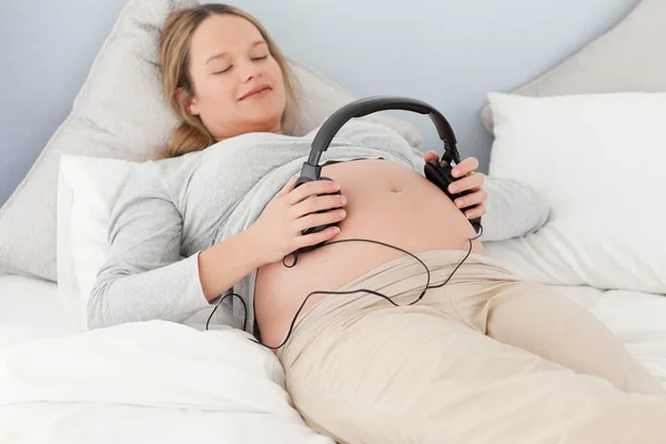 Glückliche zukünftige Mutter setzt Kopfhörer auf ihren Bauch — Stockfoto