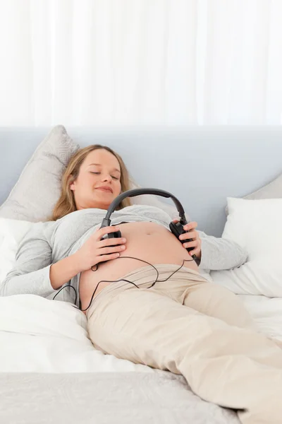 Ładny mama przyszłych umieszczenie słuchawki na brzuchu — Zdjęcie stockowe