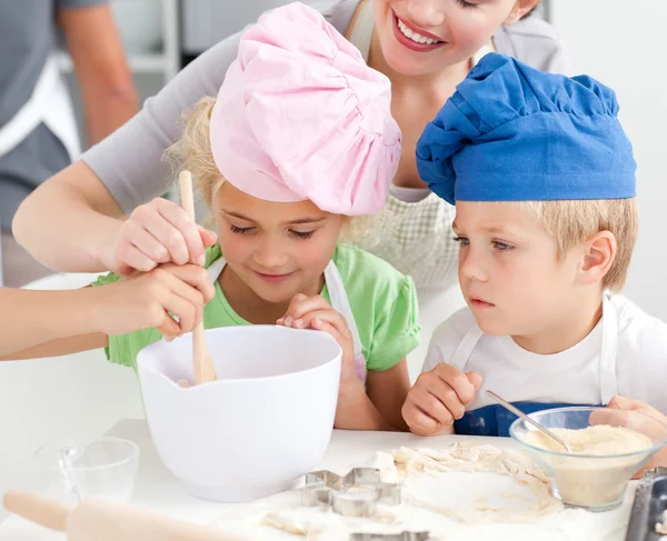 Two children and their mother stiring a preparation for cookies — Stock Photo, Image
