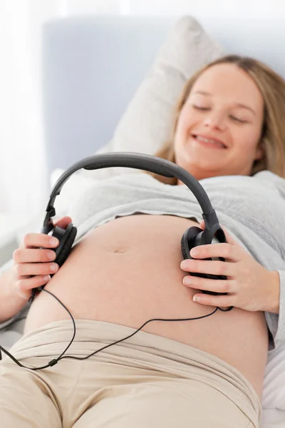 Boldog terhes nő, állítva, hogy a fejhallgató a hasában — Stock Fotó