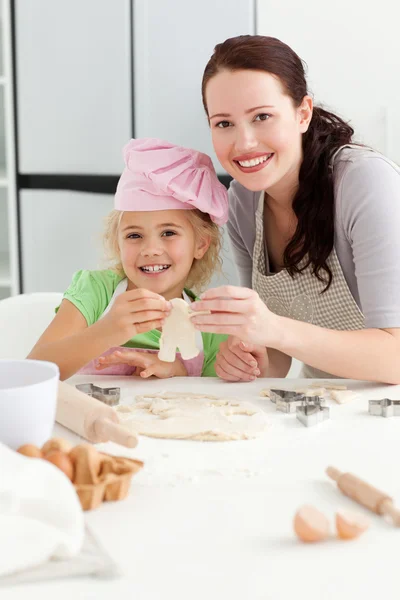 Счастливая девочка со своей матерью печет маленькие пирожки — стоковое фото