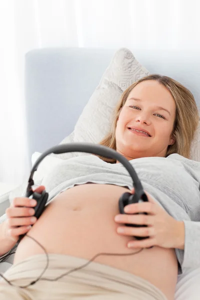 Urocza kobieta w ciąży umieszczenie słuchawki na brzuchu — Zdjęcie stockowe