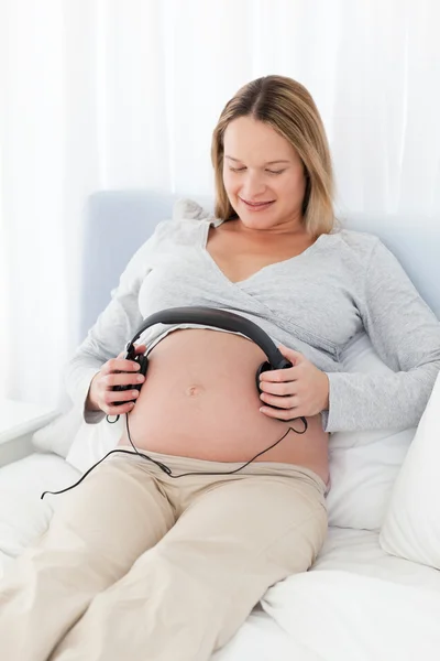 Entzückende zukünftige Mutter setzt Kopfhörer auf ihren Bauch — Stockfoto