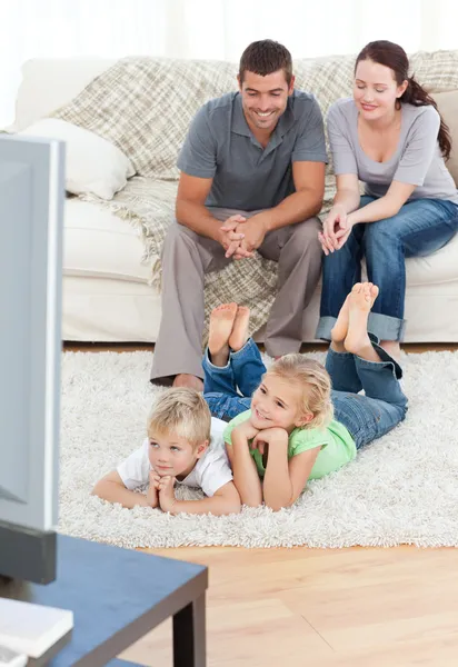 Entzückende Geschwister vor dem Fernseher mit ihren Eltern liegen o — Stockfoto