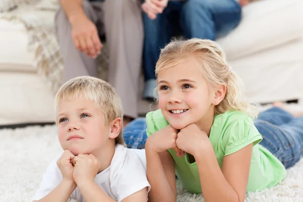 Брат и сестра смотрят телевизор на полу со своими детьми — стоковое фото