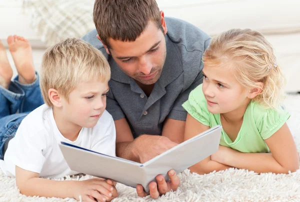 Children and father looking at a book on the floor — Stock Photo, Image