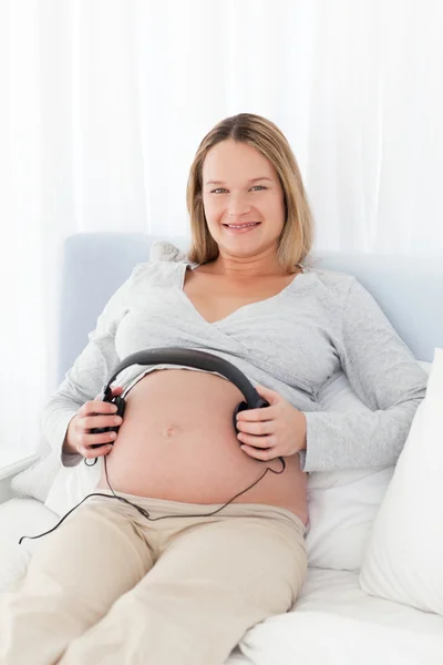 Future maman mettre des écouteurs sur son ventre — Photo