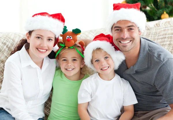 Família feliz com chapéus de Natal sentados no sofá — Fotografia de Stock