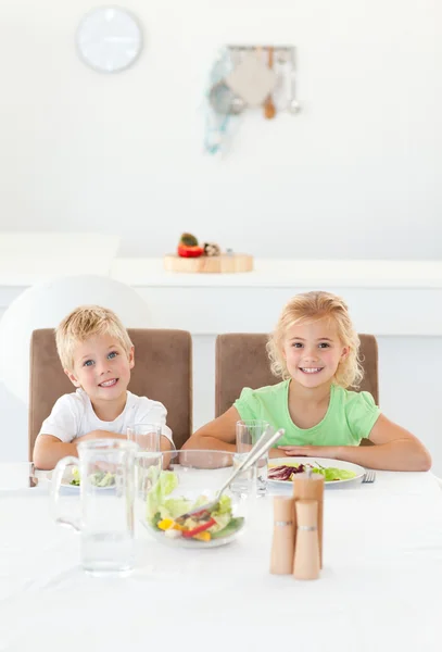 Adoráveis irmãos comendo uma salada juntos na cozinha — Fotografia de Stock