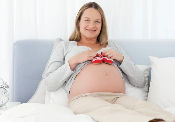 Mujer embarazada alegre poniendo zapatos de bebé en su vientre — Foto de Stock