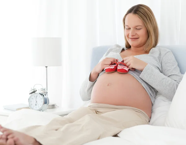 Niedliche schwangere Frau legt Babyschuhe auf ihren Bauch — Stockfoto