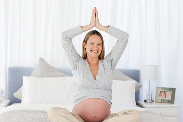 Sorridente donna incinta che fa yoga sul letto — Foto Stock
