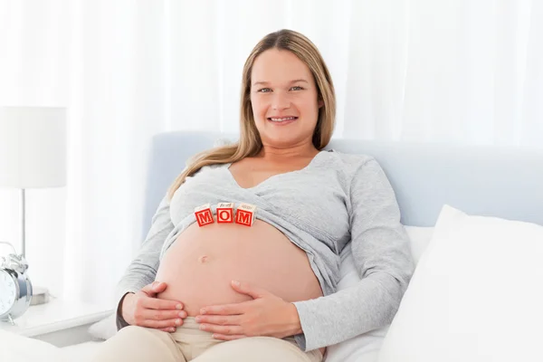 Donna incinta che riposa su un letto con le lettere della mamma — Foto Stock