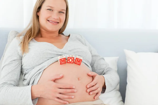 Bionda donna incinta con la mamma lettere sul suo ventre sdraiato su un be — Foto Stock
