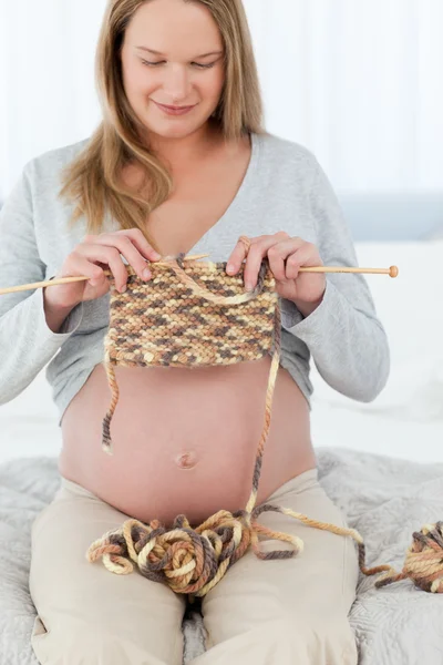 Concentrated future mom knitting sitting on a bed — Stock Photo, Image