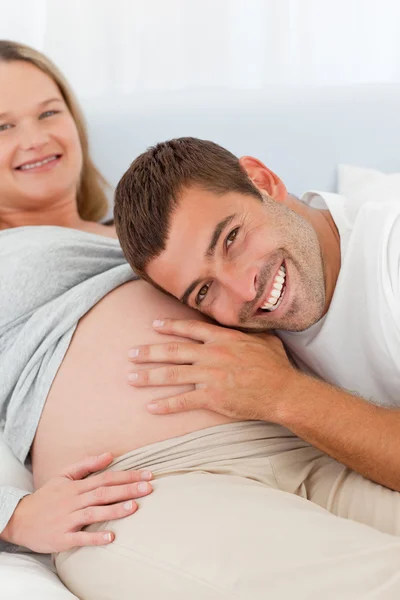 Fröhlicher Mann, der auf den Bauch seiner schwangeren Frau hört — Stockfoto