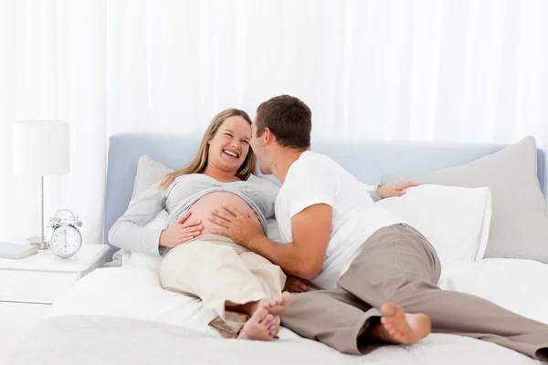 Улыбающиеся будущие родители лежат на кровати — стоковое фото