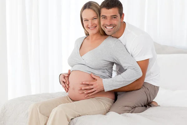 Hermosos futuros padres abrazándose sentados en el dormitorio —  Fotos de Stock
