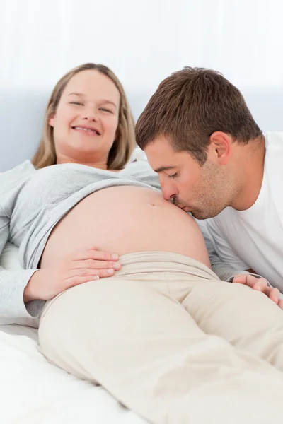 Прекрасный мужчина целует живот беременной жены в постели. — стоковое фото