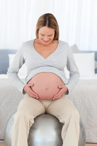 Süße schwangere Frau berührt ihren Bauch sitzend auf einem Fitnessball — Stockfoto
