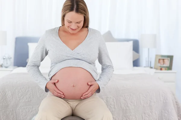 Entzückende zukünftige Mutter berührt ihren Bauch sitzend auf einem Fitnessball — Stockfoto