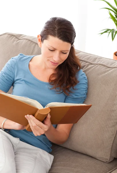 Mulher atenta lendo um livro sentado em seu sofá — Fotografia de Stock