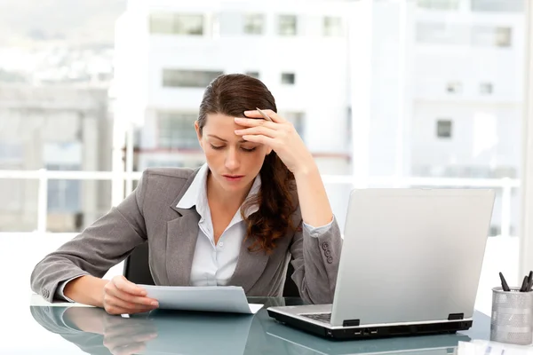 Fundersam affärskvinna tittar på ett papper när du arbetar på hennes la — Stockfoto
