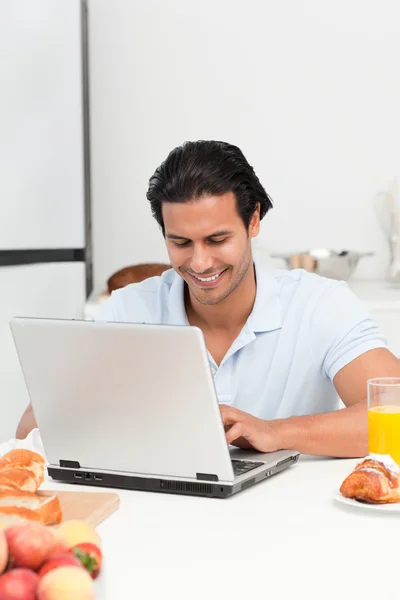 Веселий чоловік працює на ноутбуці під час закуски — стокове фото